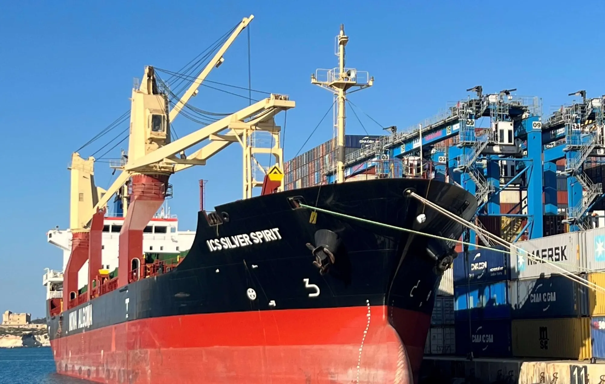 ICS Silver Spirit lying alongside a container terminal, her deck cranes stowed and shore gantries standing behind her.