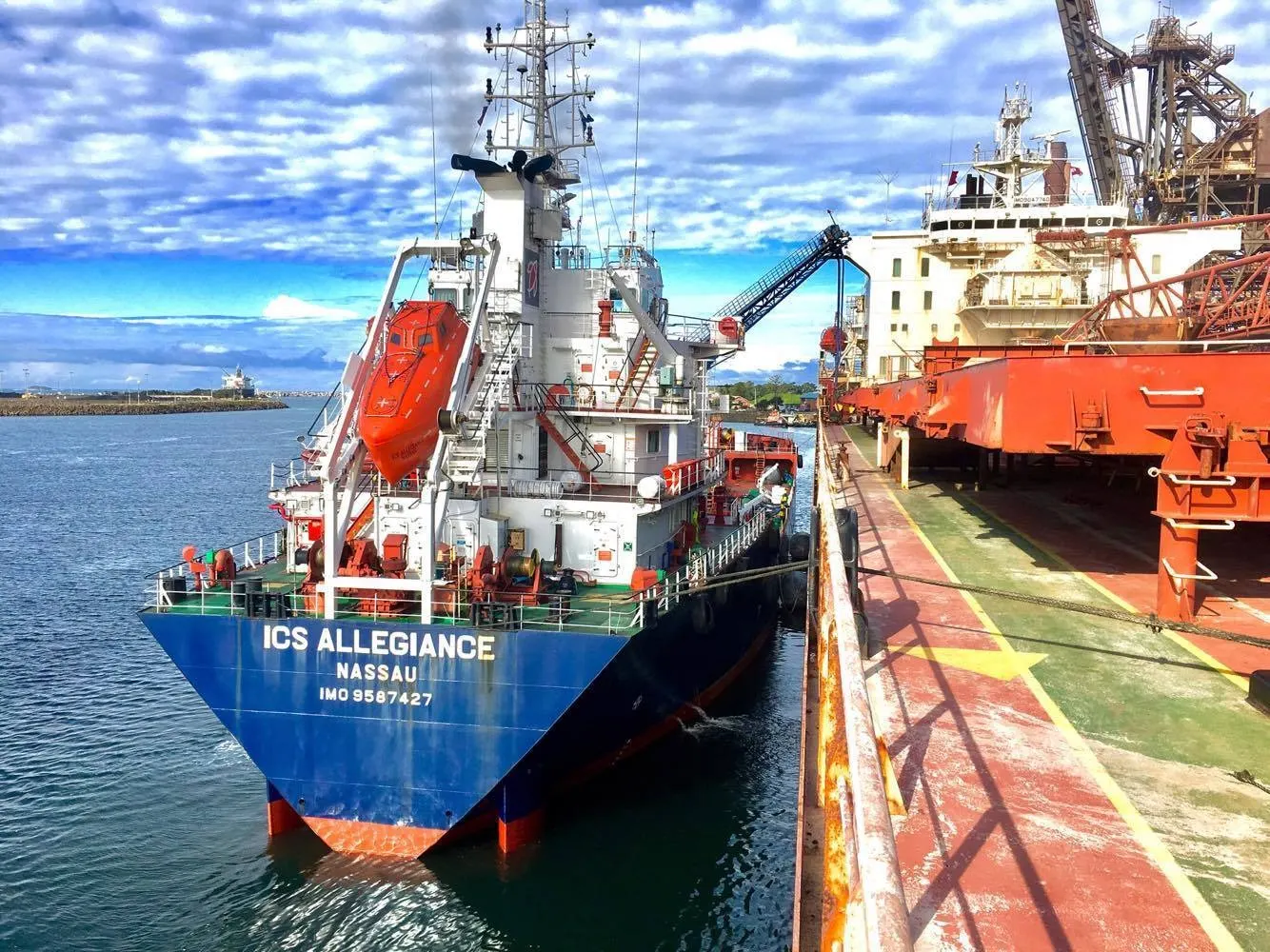 ICS Allegiance lying alongside a larger vessel with her hoses rigged, a loading berth beyond.
