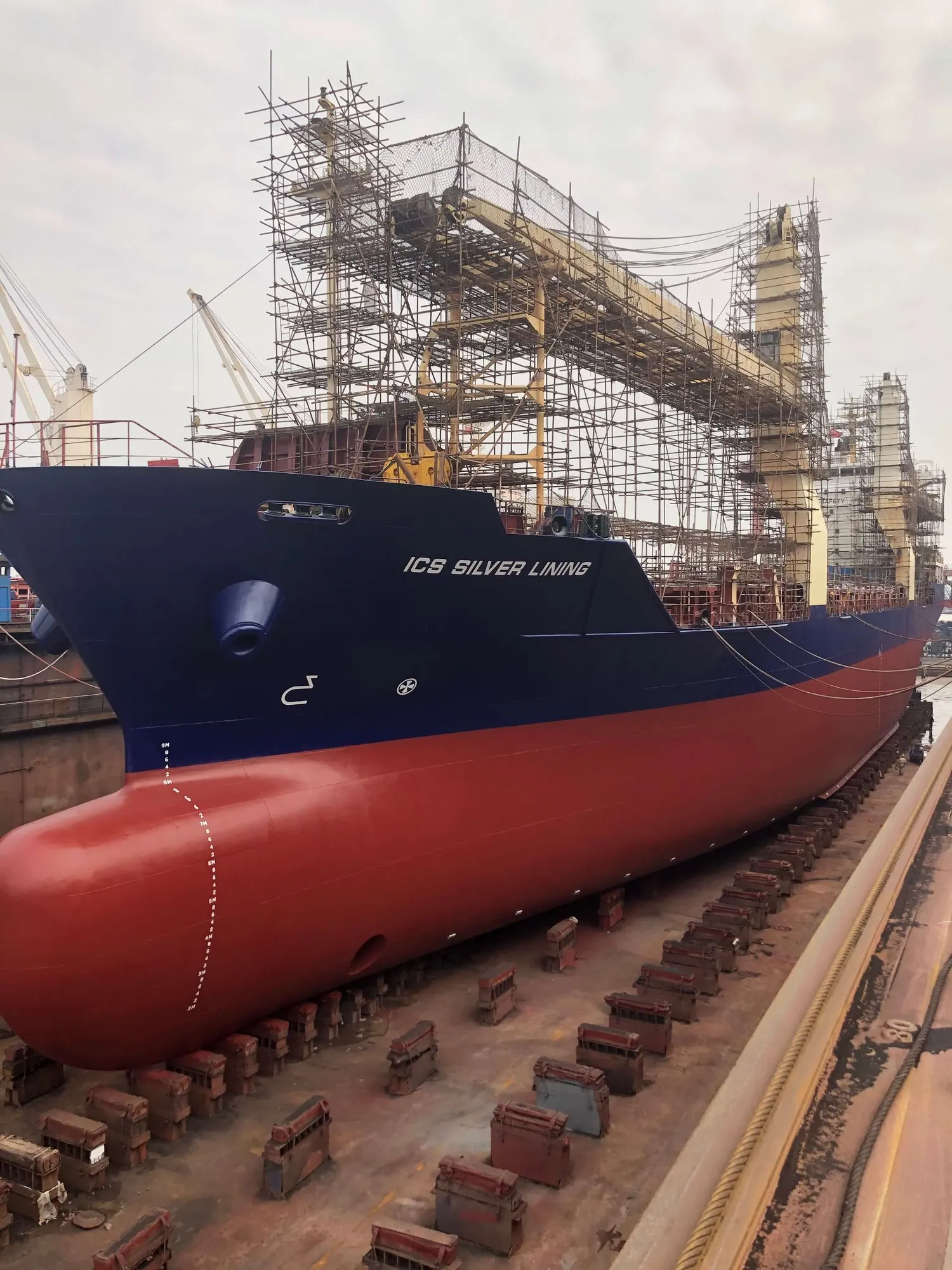 Her bow and red boot-topping standing in dry dock, scaffolding rigged over the forward deck.