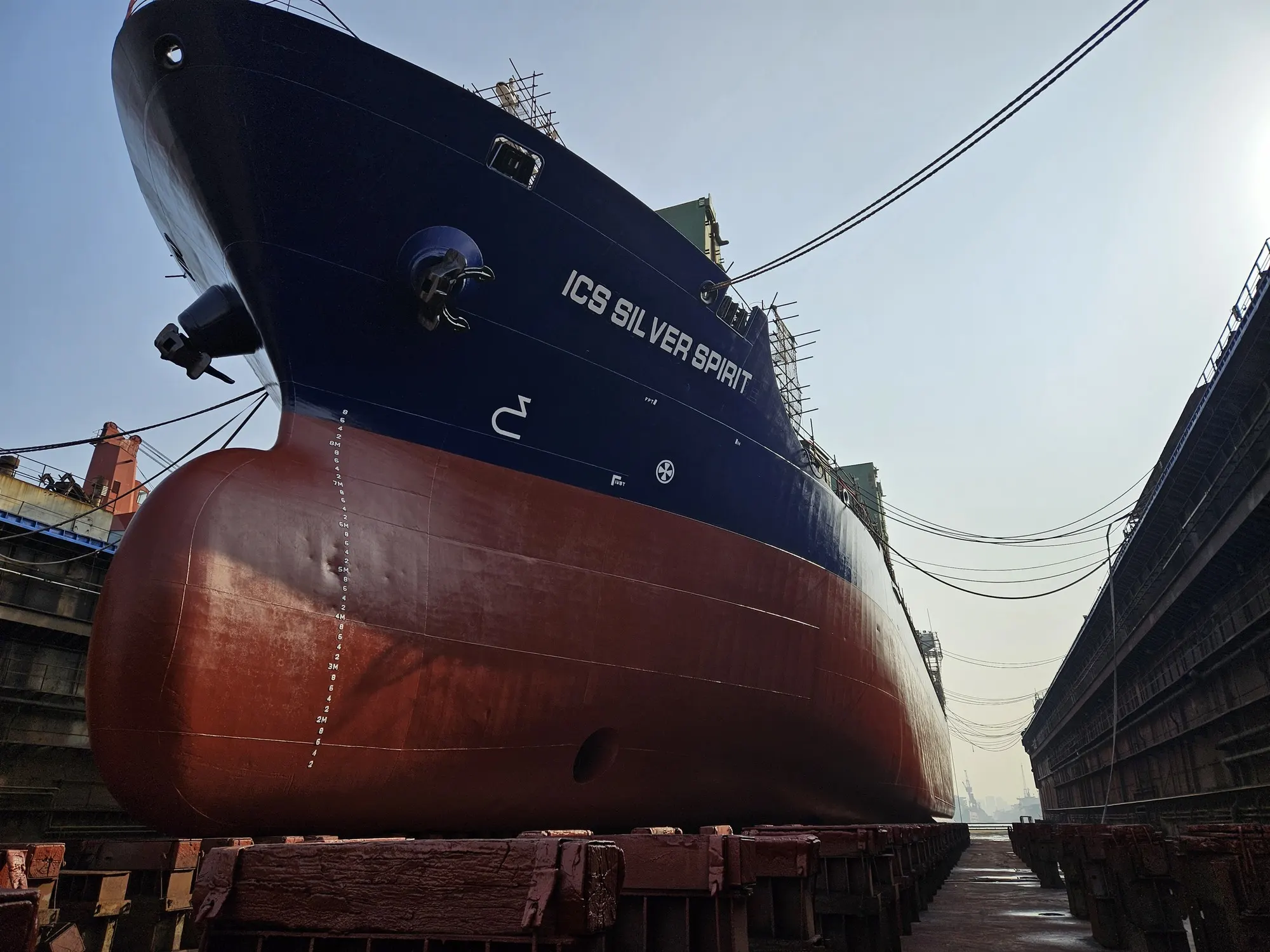 Her freshly painted bow and bulb standing on the keel blocks in dry dock, the dock wall running away aft.