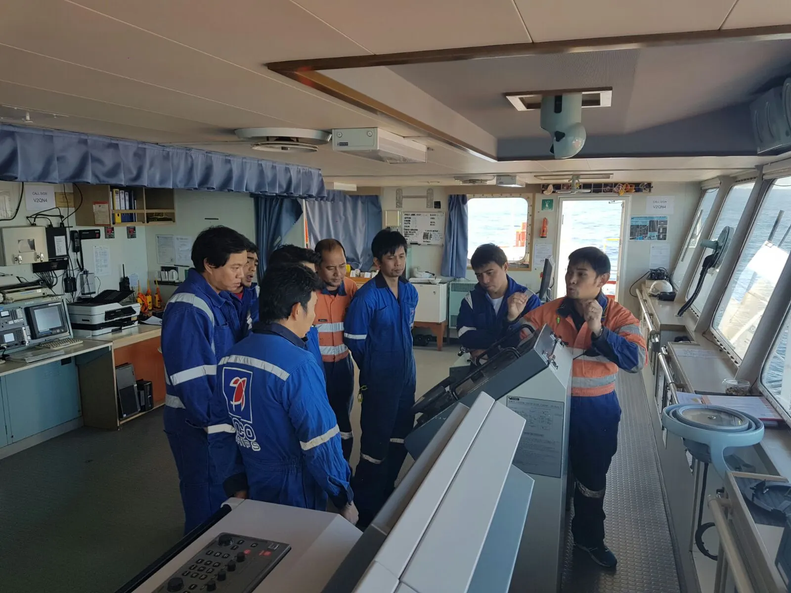 A ship’s officer briefing the crew on the bridge, gathered around the console.