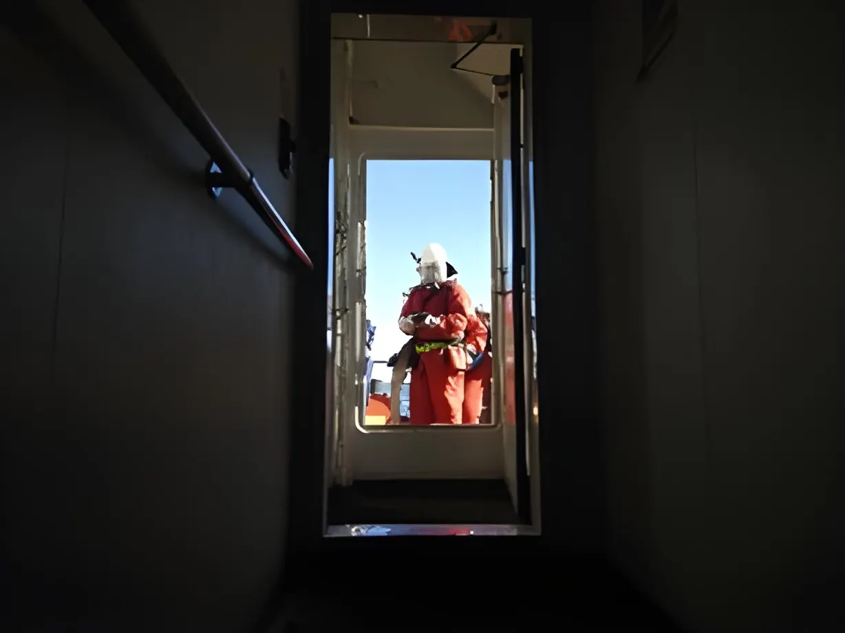 A dark internal passageway framing an open door, with a crew member in a fire suit on deck beyond.