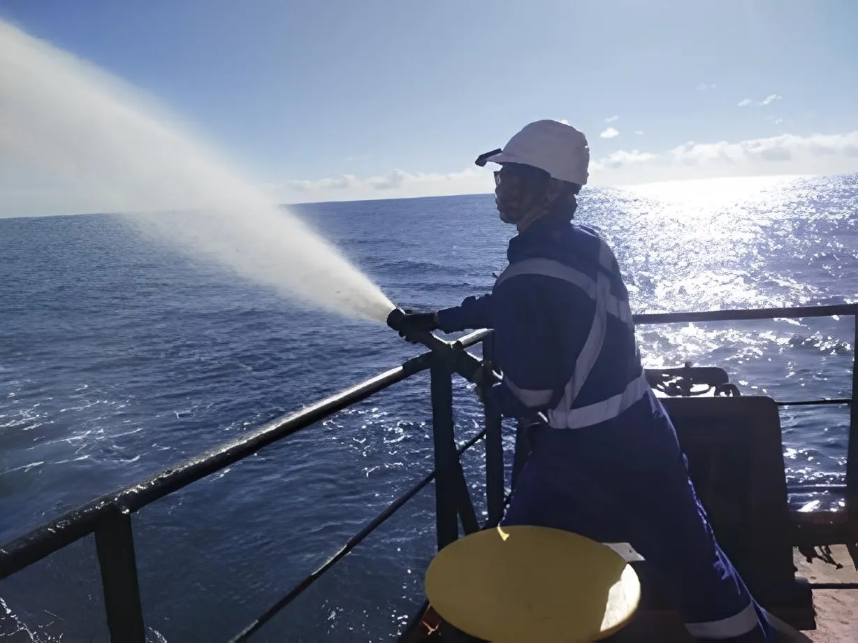 A crew member testing a fire hose over the side during a drill at sea.