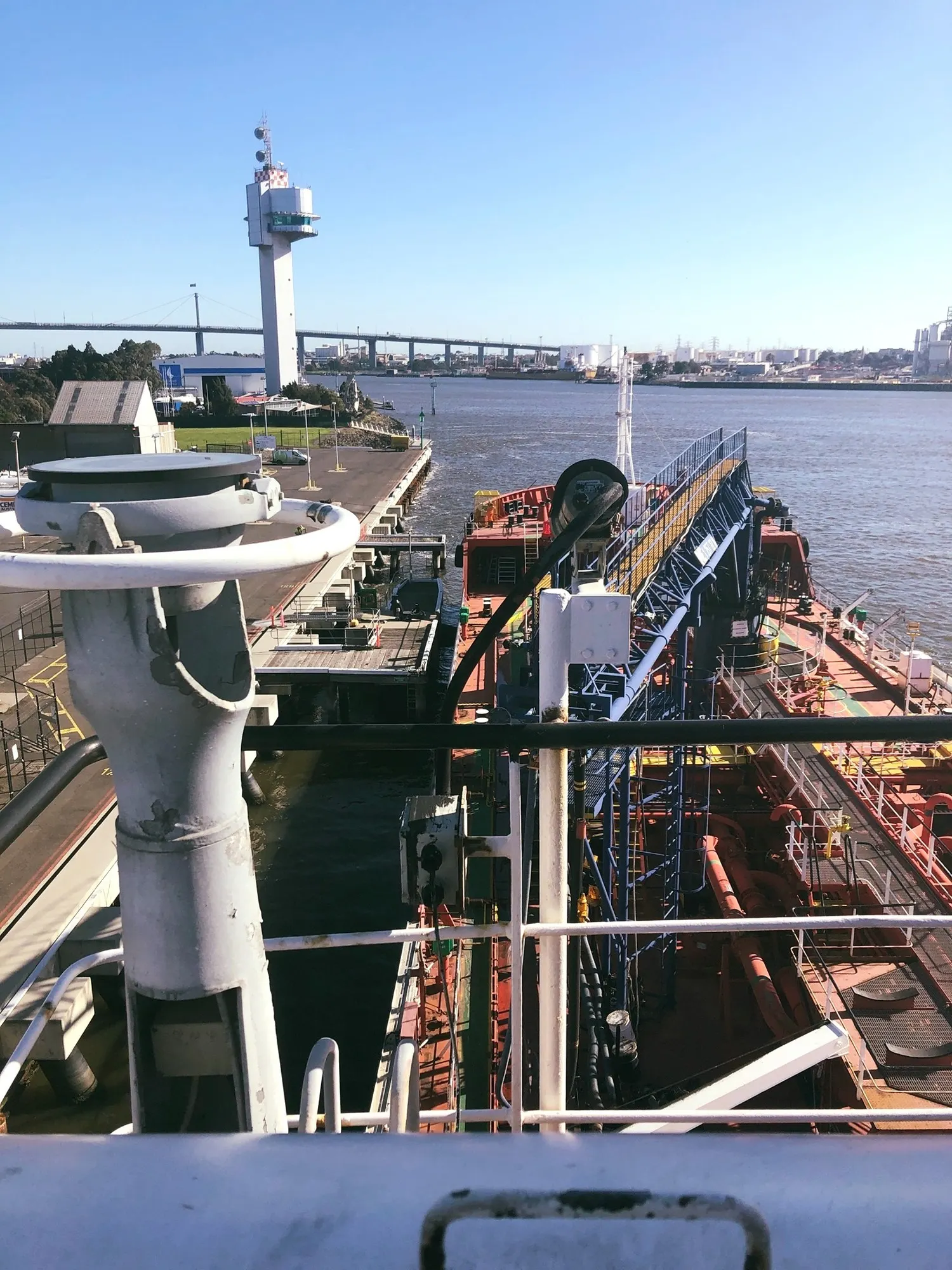 Her foredeck seen from the bridge front, hose crane and pipework in the foreground and a river bridge beyond.