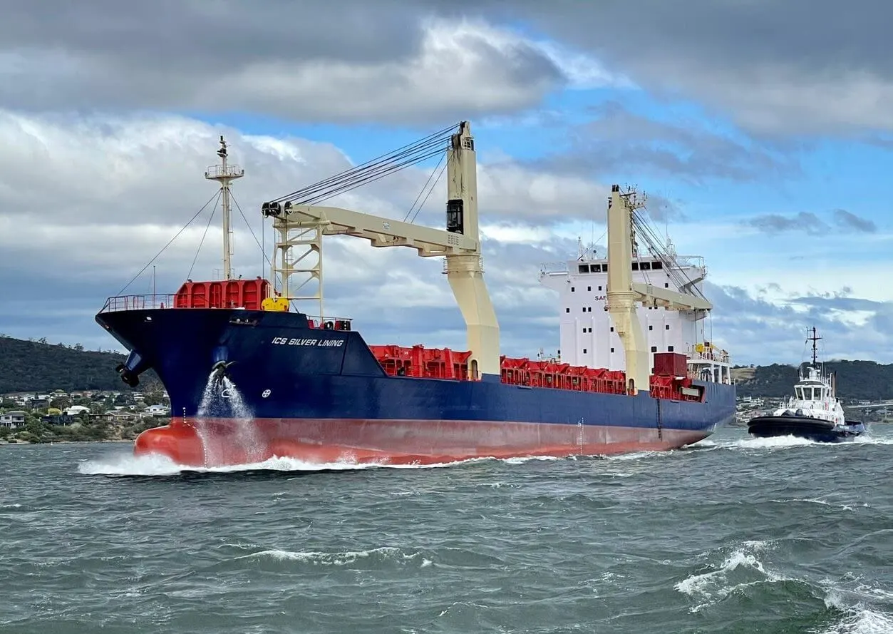 ICS Silver Lining under way with a tug alongside, her holds loaded with containers and both deck cranes standing.