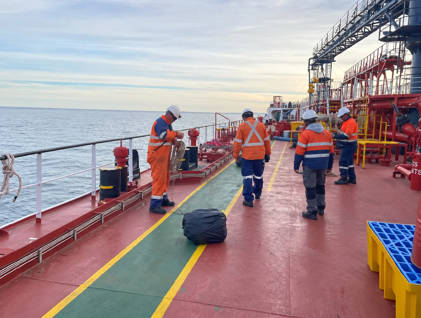 Ratings at work on a tanker’s deck, one coiling a line at the rail and others walking aft past the pipework.