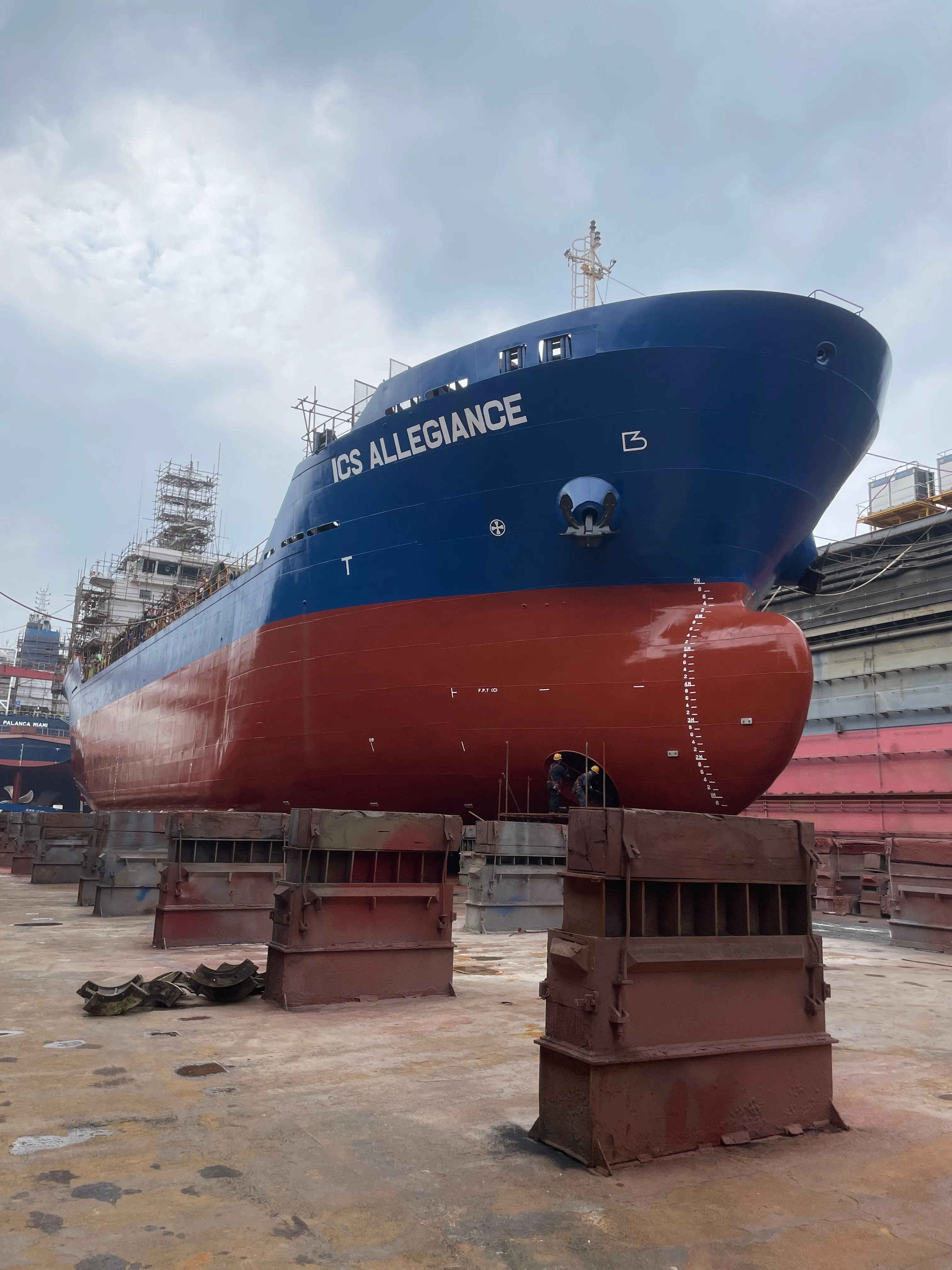 ICS Allegiance high and dry on the blocks in a dry dock, seen from ahead, with workers beneath the bow.