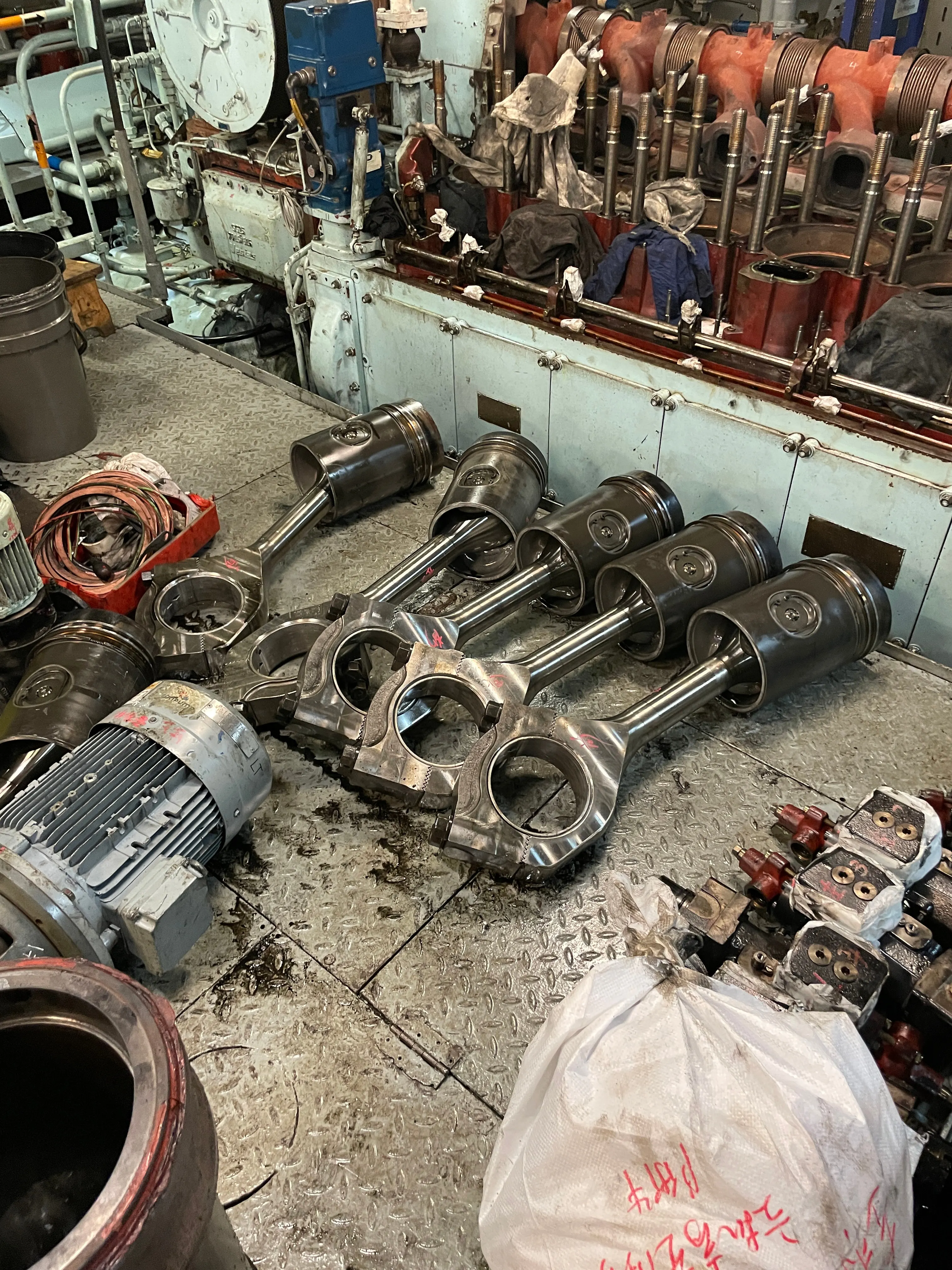 Pistons and connecting rods laid out on the engine room plates during an overhaul.